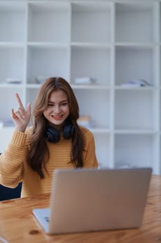 A happy young woman raises her hand during a virtual meeting with laptop.