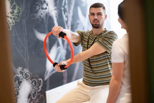 A male patient performing arm exercises using a resistance ring under supervision during a rehabilitation session.