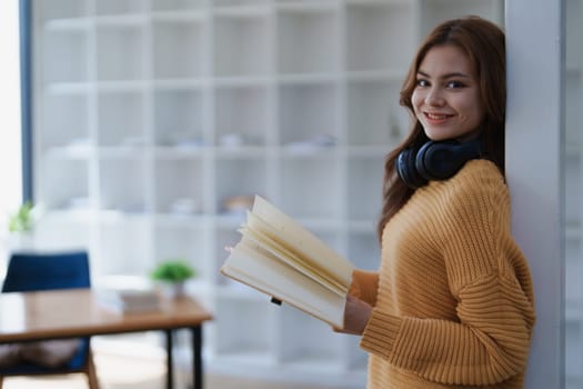 A young woman smiles while holding an open book in a bright modern office..
