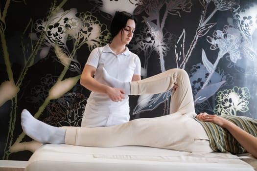 A therapist guiding a patient through leg exercises with the help of a blue foam roller in a therapy clinic.