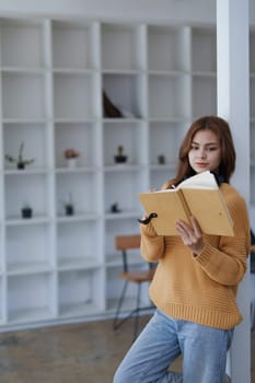 A young woman in casual clothes reads her journal leaning on a white pillar..