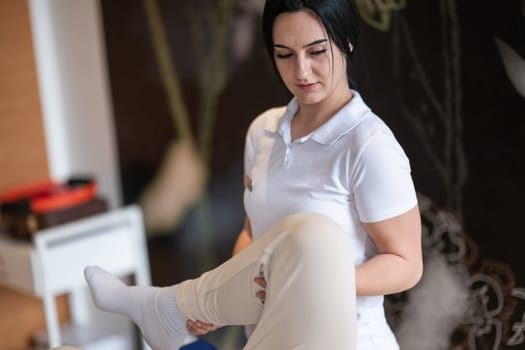 A therapist guiding a patient through leg exercises with the help of a blue foam roller in a therapy clinic.