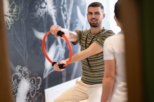 A male patient performing arm exercises using a resistance ring under supervision during a rehabilitation session.