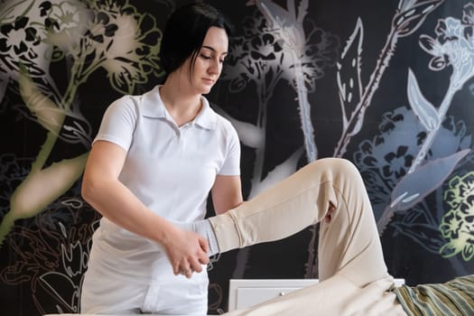 A therapist guiding a patient through leg exercises with the help of a blue foam roller in a therapy clinic.
