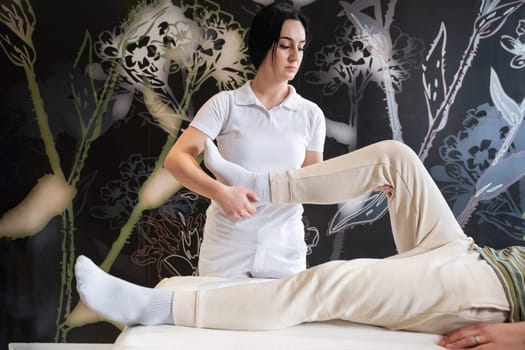 A therapist guiding a patient through leg exercises with the help of a blue foam roller in a therapy clinic.