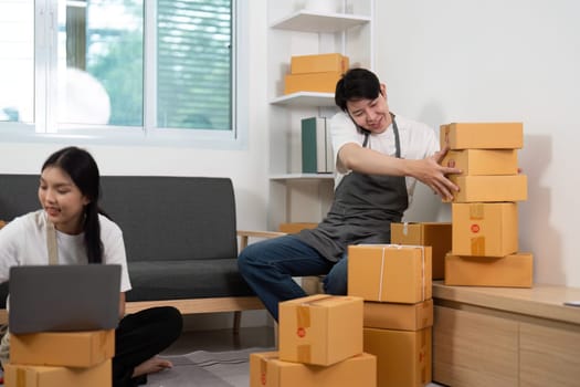 A playful couple in their home office, with one partner humorously struggling to balance stacked boxes, showcasing fun and teamwork.