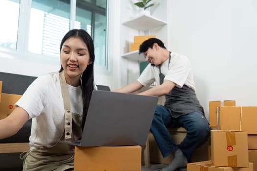 A couple shares a light moment while working on a laptop and handling packages, showcasing their partnership in a business setting.