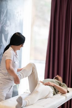 A therapist guiding a patient through leg exercises with the help of a blue foam roller in a therapy clinic.