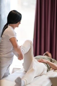 A therapist guiding a patient through leg exercises with the help of a blue foam roller in a therapy clinic.