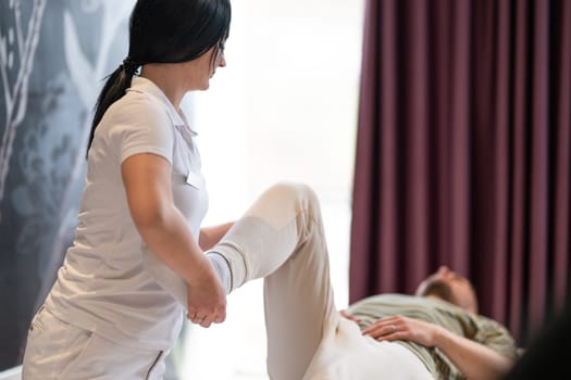 A therapist guiding a patient through leg exercises with the help of a blue foam roller in a therapy clinic.