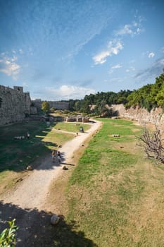 Rodas.Greece - june 04, 2025: Expansive view of the medieval moats and formidable stone walls surrounding the historic city of Rhodes under a bright sky.