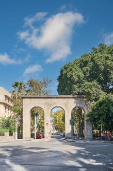Rodas.Greece - june 04, 2025: Dynamic street scene in Rhodes, featuring an ancient stone arch serving as a gateway to bustling urban activity.