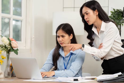 Two businesswomen analyze data on a laptop, demonstrating teamwork and problem-solving in a modern workspace.