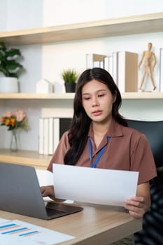 A professional woman analyzing important documents while working on her laptop, emphasizing focus and dedication in her workspace.