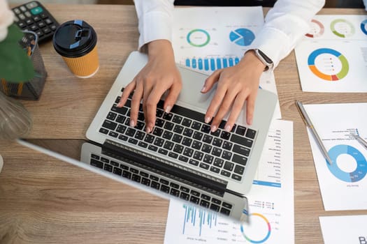 A business professional engaged in remote work, analyzing financial graphs and reports on a laptop, showcasing productivity and focus.