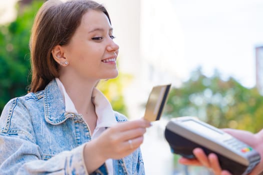 Caucasian woman smiling as she pays with a credit card using contactless technology at an outdoor cafe. A casual urban moment reflecting convenience, lifestyle, and modern financial habits.