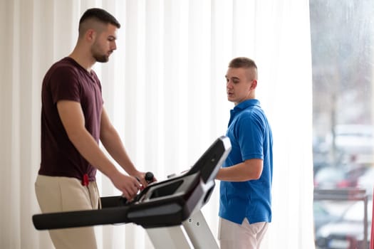 Man undergoing physical therapy with trainer assistance on a treadmill indoors.