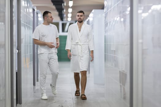 Medical Consultation in Spa Corridor.Two men discussing treatment options while walking through a clinical spa corridor, wearing white uniforms and bathrobe