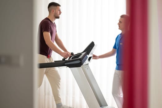 Man undergoing physical therapy with trainer assistance on a treadmill indoors.
