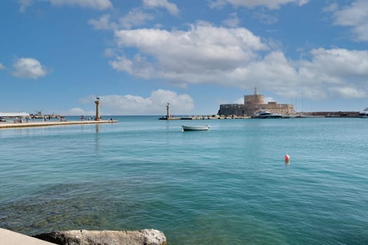 Rodas.Greece - june 04, 2025: Panoramic view of Mandraki Harbour in Rhodes, featuring the historic Fort of Saint Nicholas and its iconic lighthouses under a blue sky.