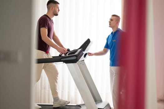 Man undergoing physical therapy with trainer assistance on a treadmill indoors.