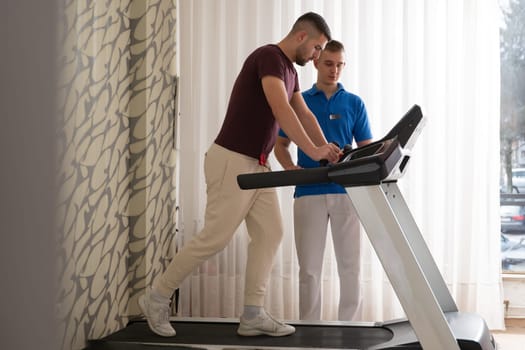 Man undergoing physical therapy with trainer assistance on a treadmill indoors.