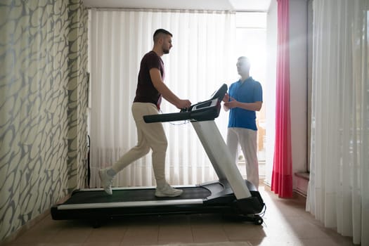 Man undergoing physical therapy with trainer assistance on a treadmill indoors.