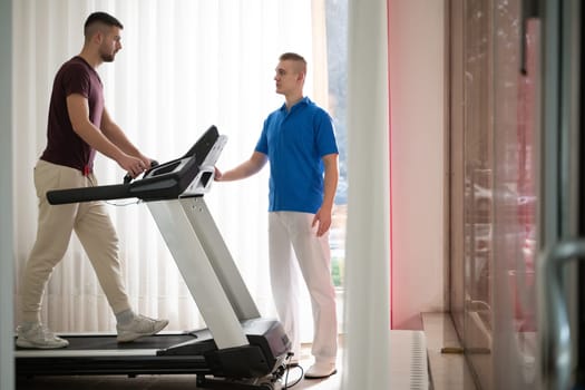 Man undergoing physical therapy with trainer assistance on a treadmill indoors.
