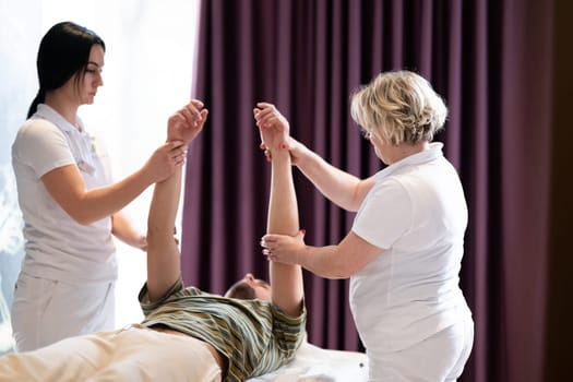 Physical Therapy Session with Two Therapists. Two therapists assist a male patient in a physiotherapy session, focusing on arm rehabilitation exercises.