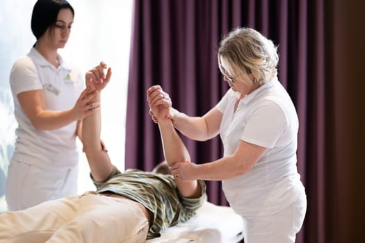 Physical Therapy Session with Two Therapists. Two therapists assist a male patient in a physiotherapy session, focusing on arm rehabilitation exercises.