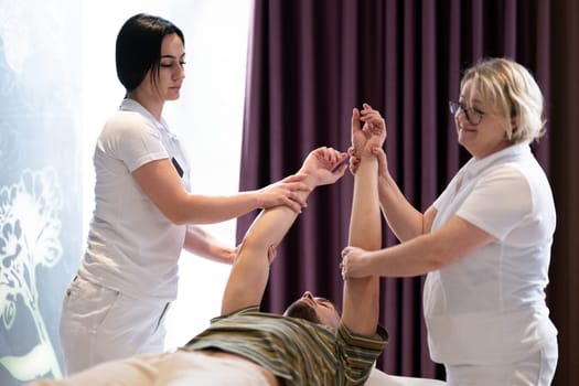 Physical Therapy Session with Two Therapists. Two therapists assist a male patient in a physiotherapy session, focusing on arm rehabilitation exercises.