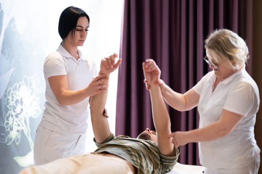 Physical Therapy Session with Two Therapists. Two therapists assist a male patient in a physiotherapy session, focusing on arm rehabilitation exercises.
