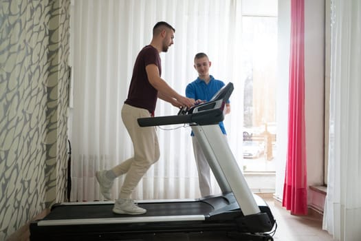 Man undergoing physical therapy with trainer assistance on a treadmill indoors.