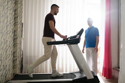 Man undergoing physical therapy with trainer assistance on a treadmill indoors.