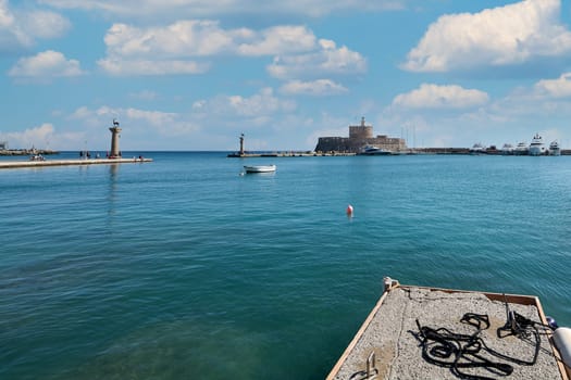 Serene and picturesque scene of Rhodes' famous Mandraki port, with historical landmarks and serene waters, perfect for relaxation.