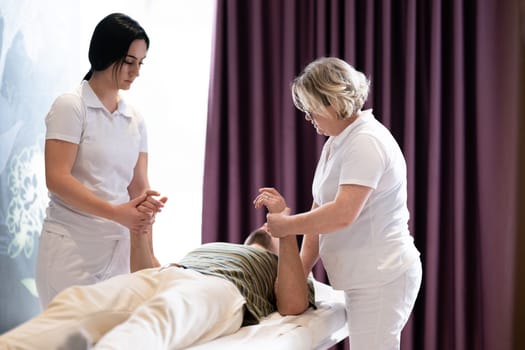 Physical Therapy Session with Two Therapists. Two therapists assist a male patient in a physiotherapy session, focusing on arm rehabilitation exercises.
