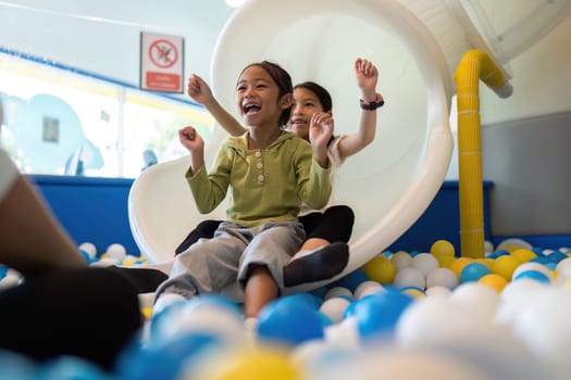 Two girls gleefully sliding down a playground slide, surrounded by colorful balls, embodying the joy of childhood play.