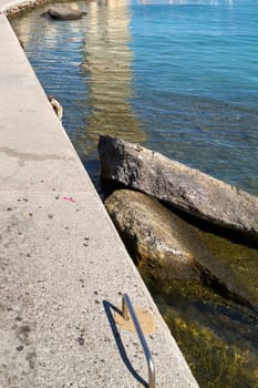 Close-up of a concrete pier with visible rocks and steps leading into the tranquil, clear waters of Rhodes.