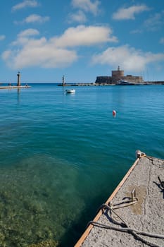 Panoramic view of Mandraki Harbour, showcasing the historic Fort of Saint Nicholas, distant lighthouses, and crystal-clear waters.
