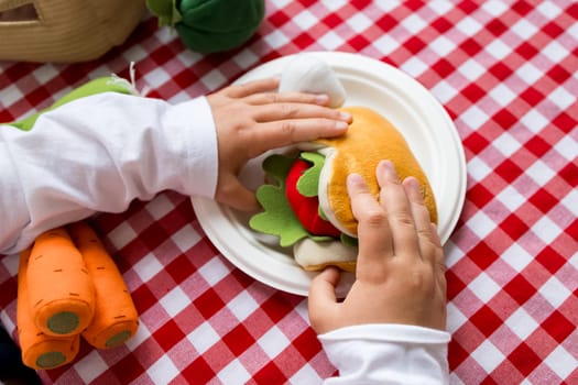 Child playing with toy sandwich on red checkered tablecloth.