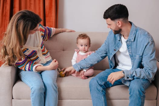 Smiling parents sitting on a sofa while playing with their baby girl using a toy ball. Warm indoor setting ideal for themes like love, family bonding, early development, and parenting.