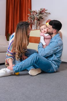 Touching family moment with father holding and kissing his baby girl as mother looks on. Captured in a cozy indoor space, ideal for themes like love, childhood, parenting, and emotional bonds.Vertical