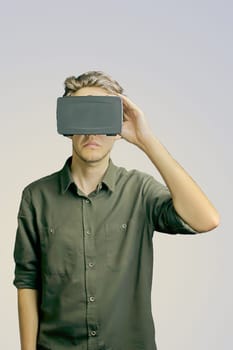 Young man in a shirt uses virtual reality glasses on the light grey background