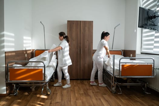 Two nurses in uniforms cleaning and organizing a hospital room by changing the bed linens and ensuring a hygienic environment for patients