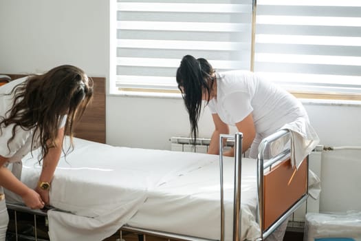 Two nurses in uniforms cleaning and organizing a hospital room by changing the bed linens and ensuring a hygienic environment for patients