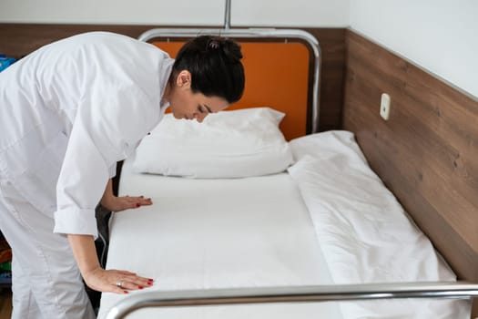 Two nurses in uniforms cleaning and organizing a hospital room by changing the bed linens and ensuring a hygienic environment for patients
