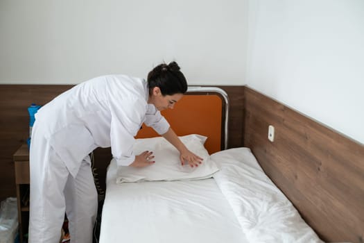 Two nurses in uniforms cleaning and organizing a hospital room by changing the bed linens and ensuring a hygienic environment for patients