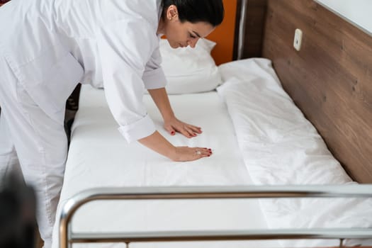 Two nurses in uniforms cleaning and organizing a hospital room by changing the bed linens and ensuring a hygienic environment for patients