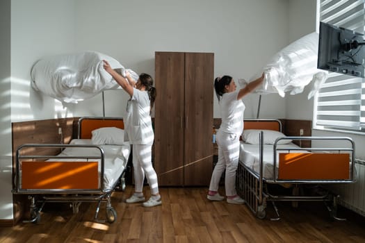 Two nurses in uniforms cleaning and organizing a hospital room by changing the bed linens and ensuring a hygienic environment for patients