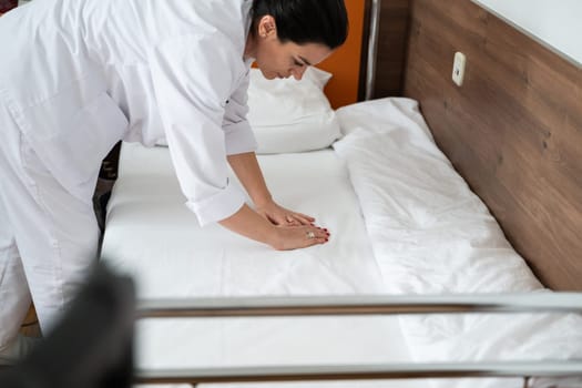 Two nurses in uniforms cleaning and organizing a hospital room by changing the bed linens and ensuring a hygienic environment for patients